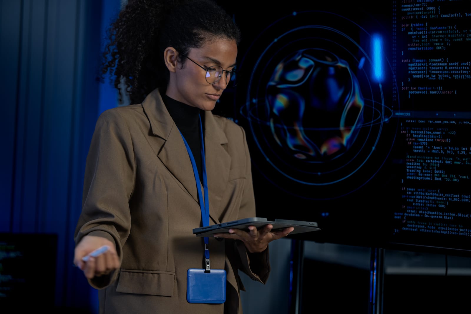 Specialist working on a tablet in front of dark screens with code